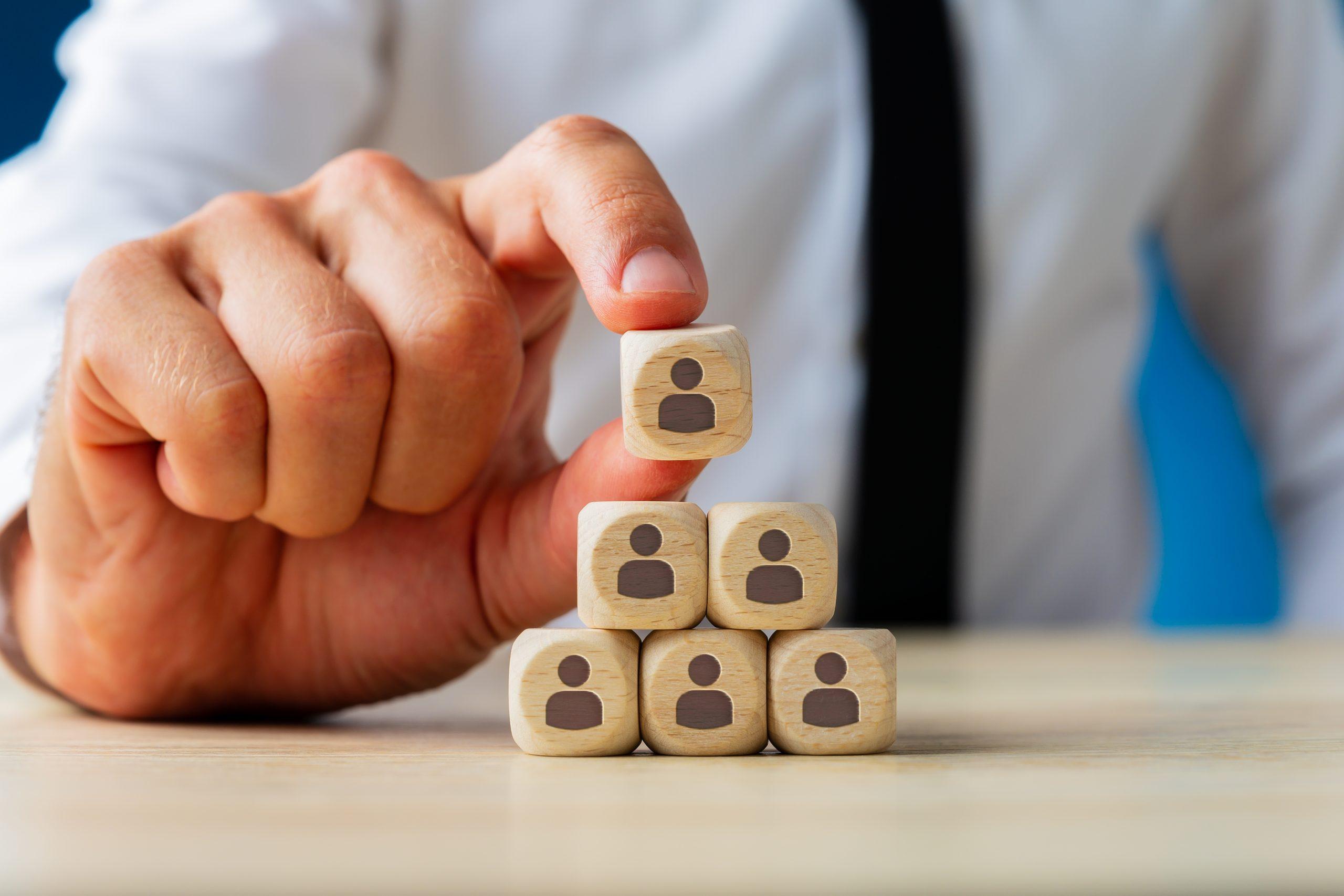 Business executive stacking wooden dices  with people icons on them in a pyramid shape in a conceptual image.